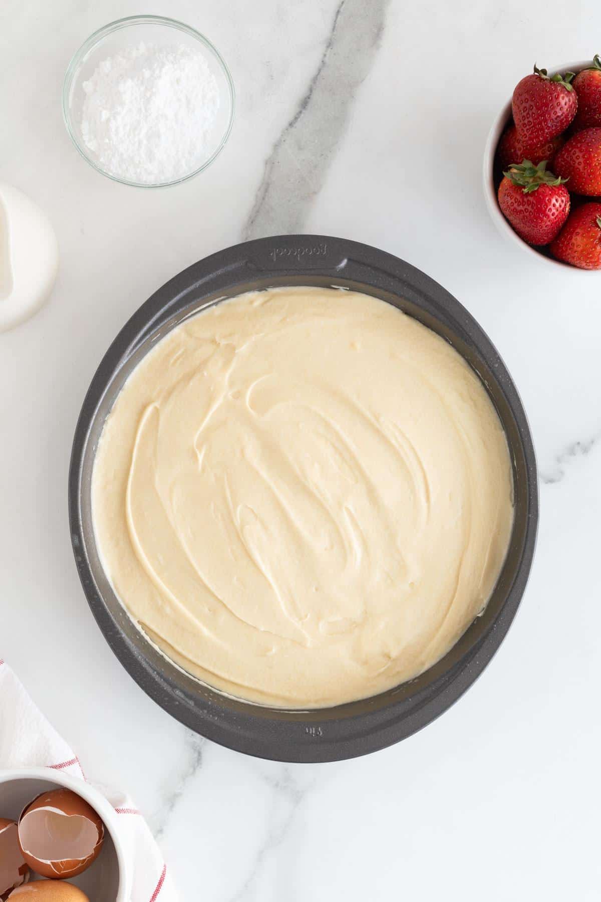 Cake batter in a round baking pan, with surrounding baking ingredients