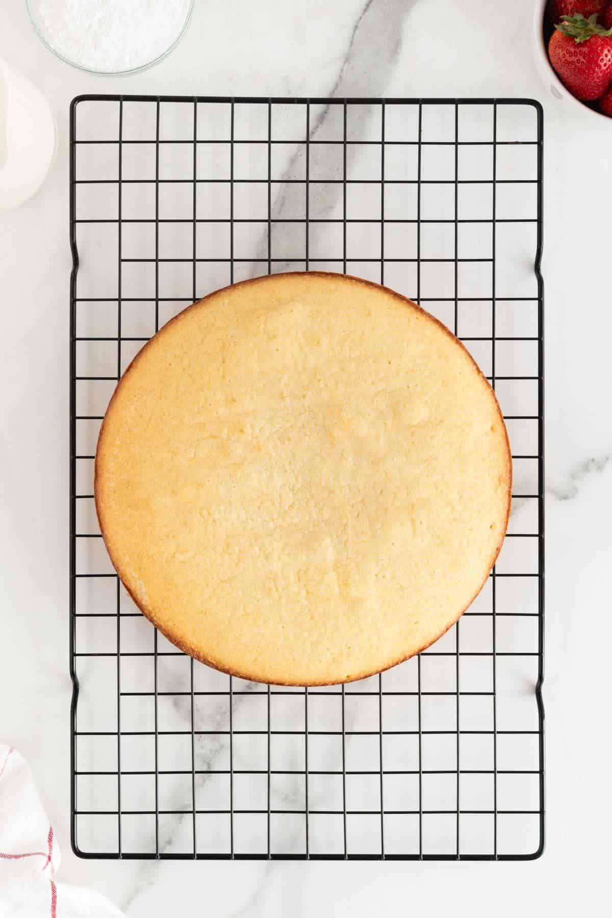 A baked round cake cooling on a wire rack, viewed from above