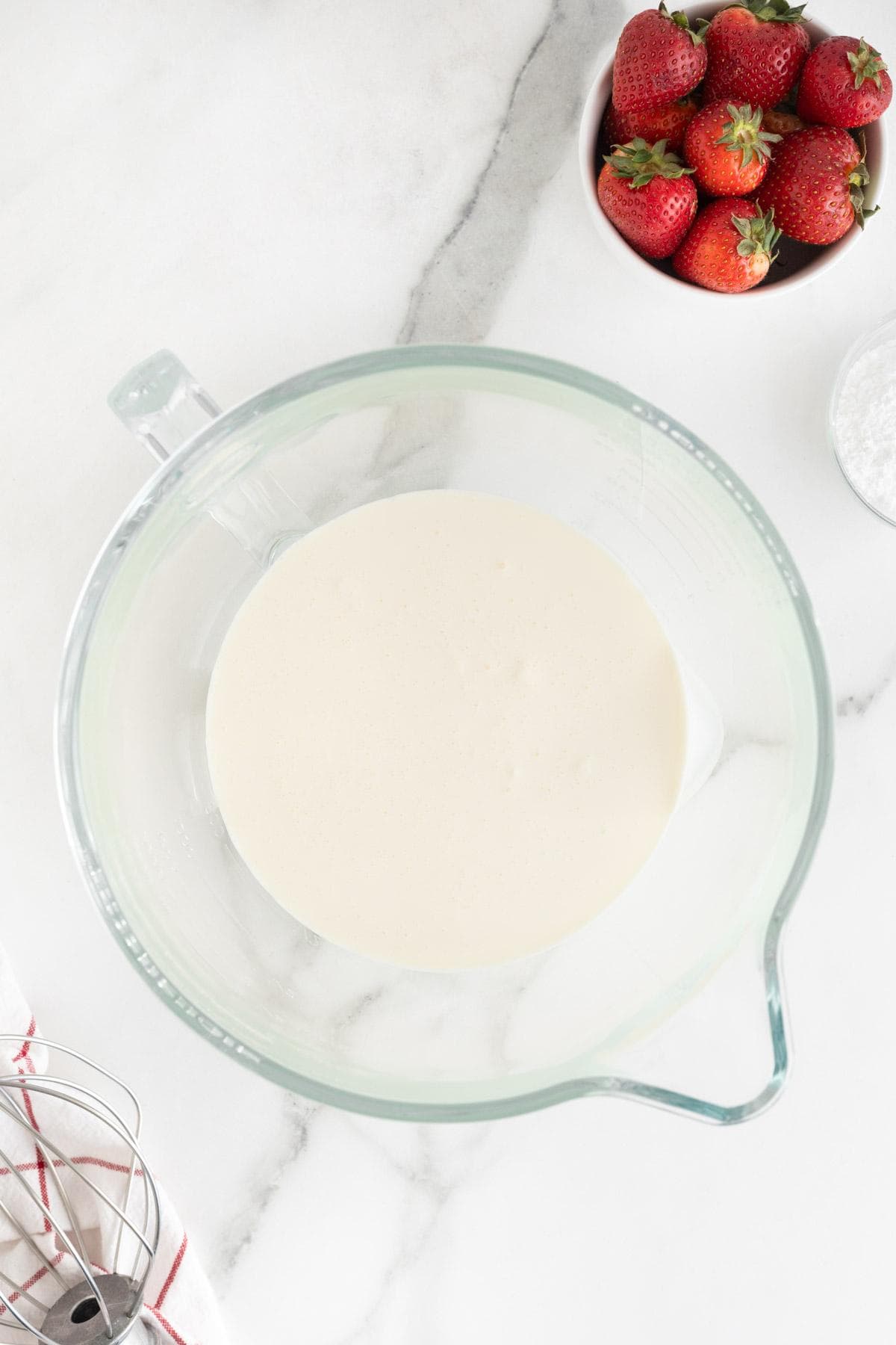 Whipped cream in a glass bowl, with strawberries nearby