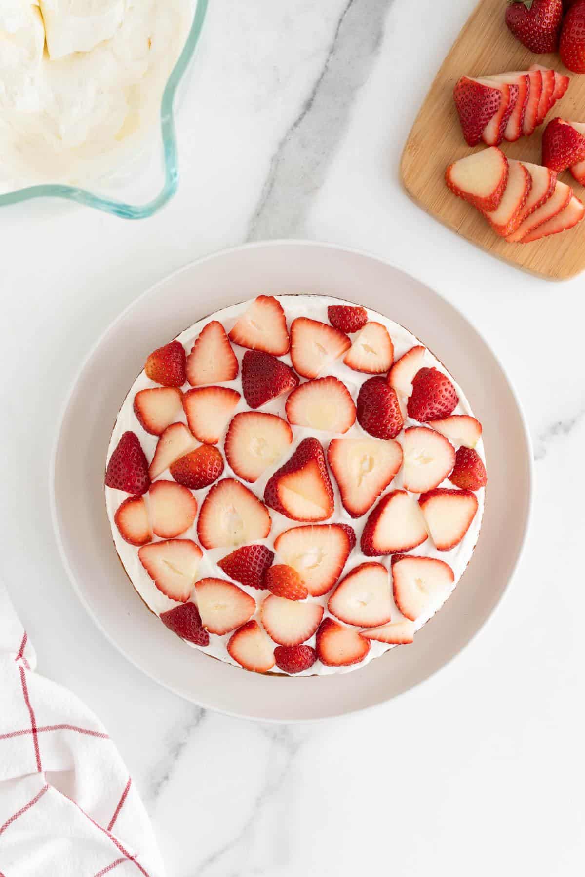 A cake layer topped with whipped cream and evenly placed sliced strawberries