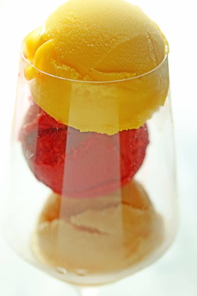 Close up of a wine glass containing mango, strawberry and peach sorbet without the ginger ale