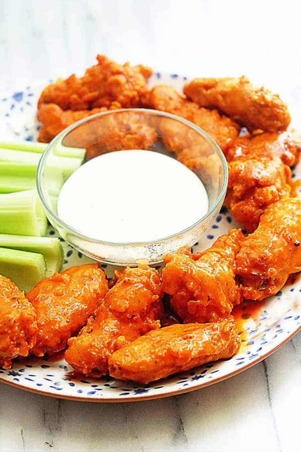 A plate full of the best buffalo wings on the table with celery and dipping sauce.