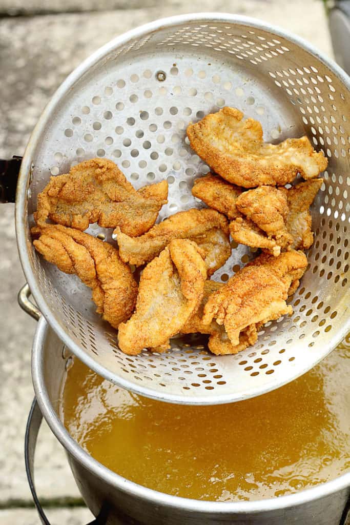 Photo of fried fish hanging over a deep fryer full of cooking oil