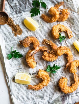 Overhead shot of Fried shrimp seasoned in cornmeal and fried to a golden brown with lemon slices and seasoning on top of newspaper