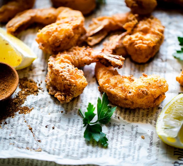 Close up of Fried shrimp seasoned in cornmeal and fried to a golden brown with lemon slices and seasoning on top of newspaper