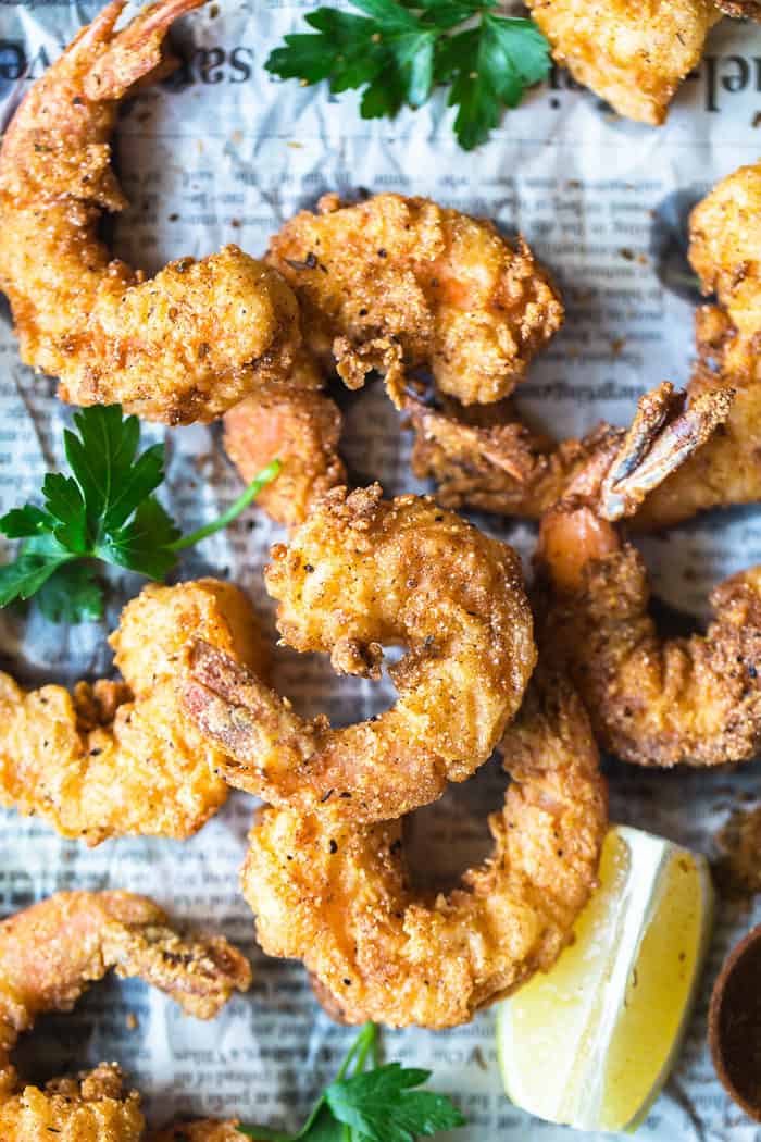 Overhead shot of a close up of Fried shrimp seasoned in cornmeal and fried to a golden brown with lemon slices on top of newspaper