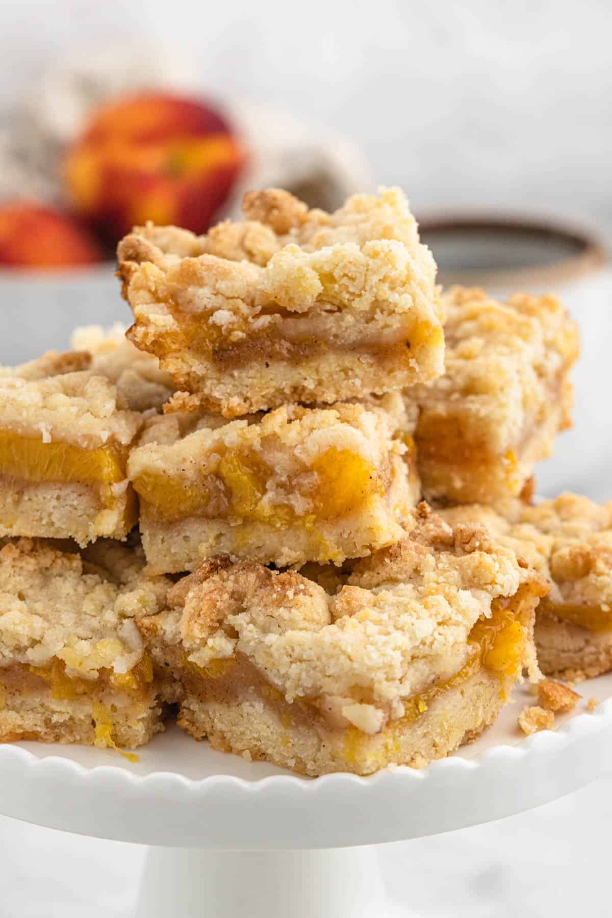 Homemade peach crumb bars cut and stacked on a white plate.