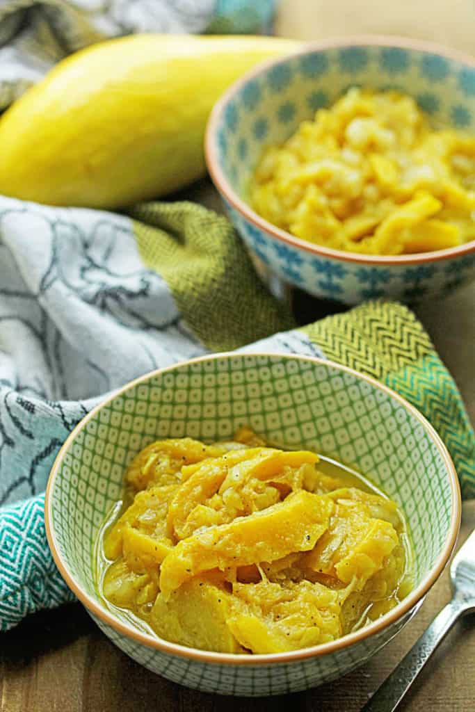 Close up of one bowl of sauteed yellow squash with another bowl of it in the background along with a whole yellow squash