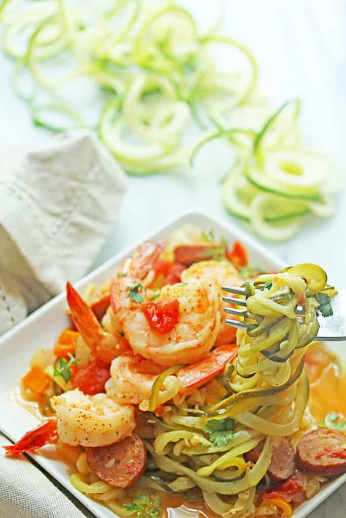 Close up of Cajun Shrimp Zoodles served on a square, white plate with a fork holding vegetable noodles