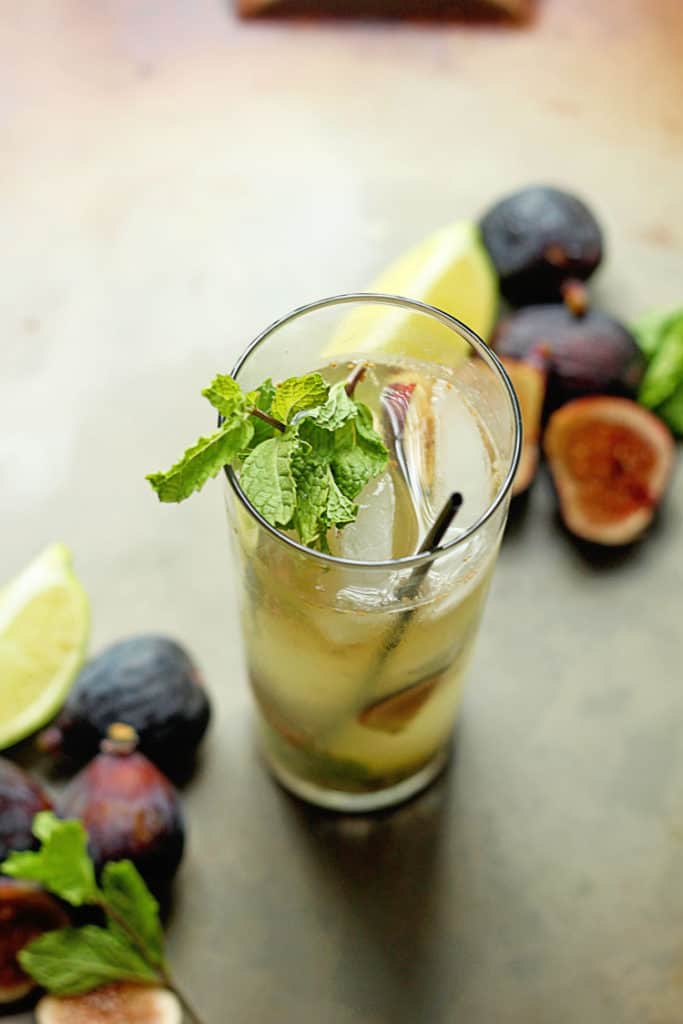Overhead shot of a fig mojito with a skinny, black straw and mint in it and sliced figs and lemon around it