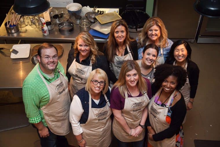Group photo of Jocelyn Delk Adams and fellow food bloggers wearing aprons in a test kitchen