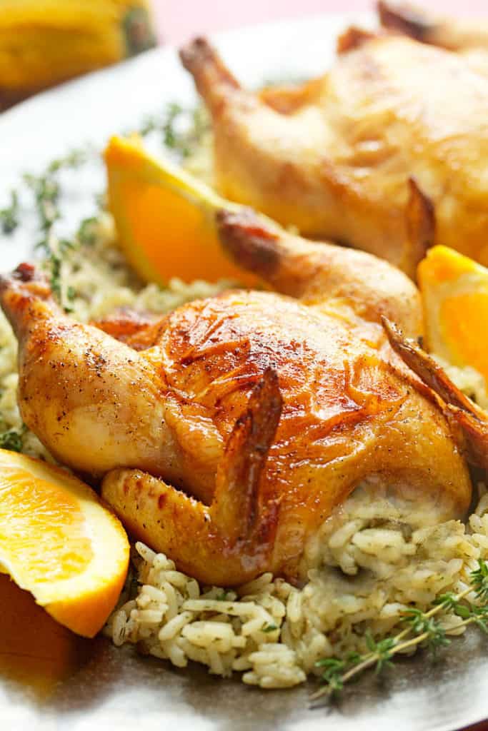 Close up of a Coca-Cola Glazed Cornish Hen sitting on top of a bed of cooked rice and orange wedges