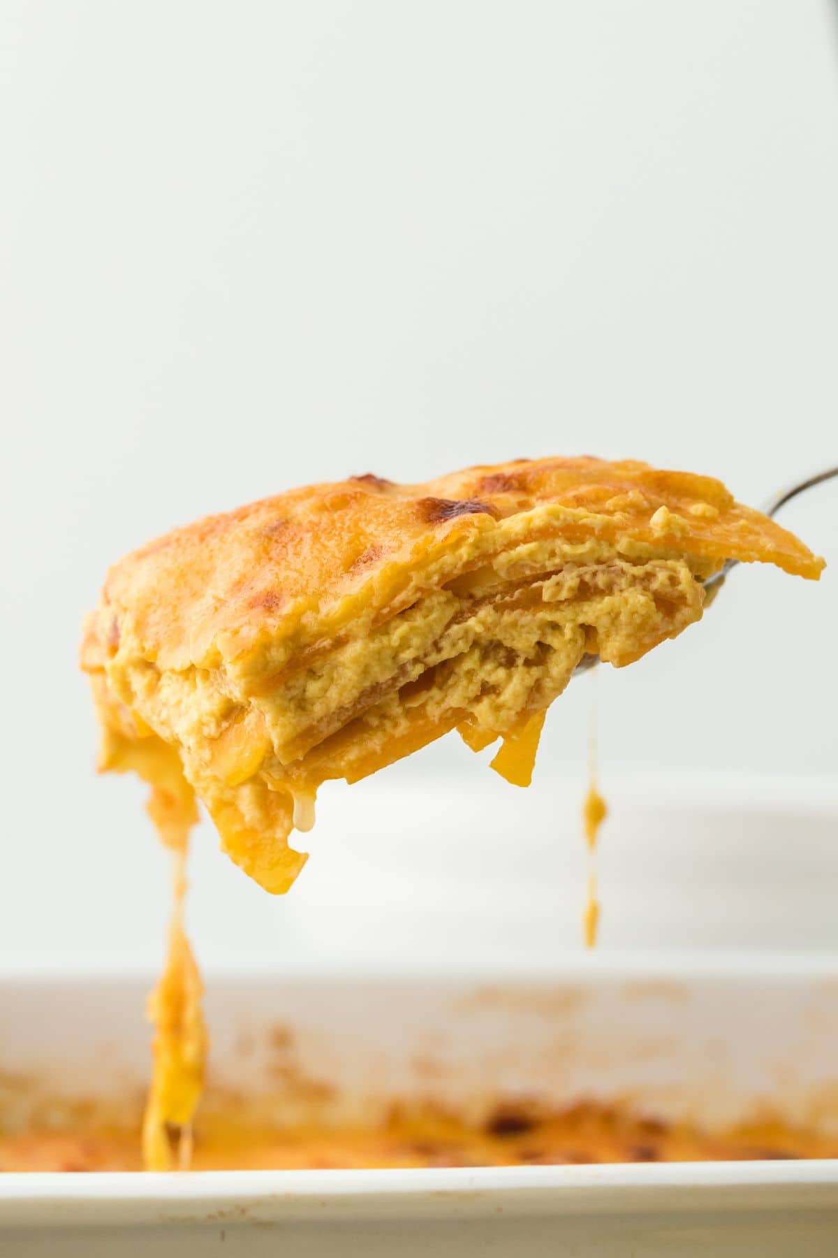 Closeup of a cheesy slice of potato and squash gratin being lifted from the baking dish, with cheese stretching as it's pulled