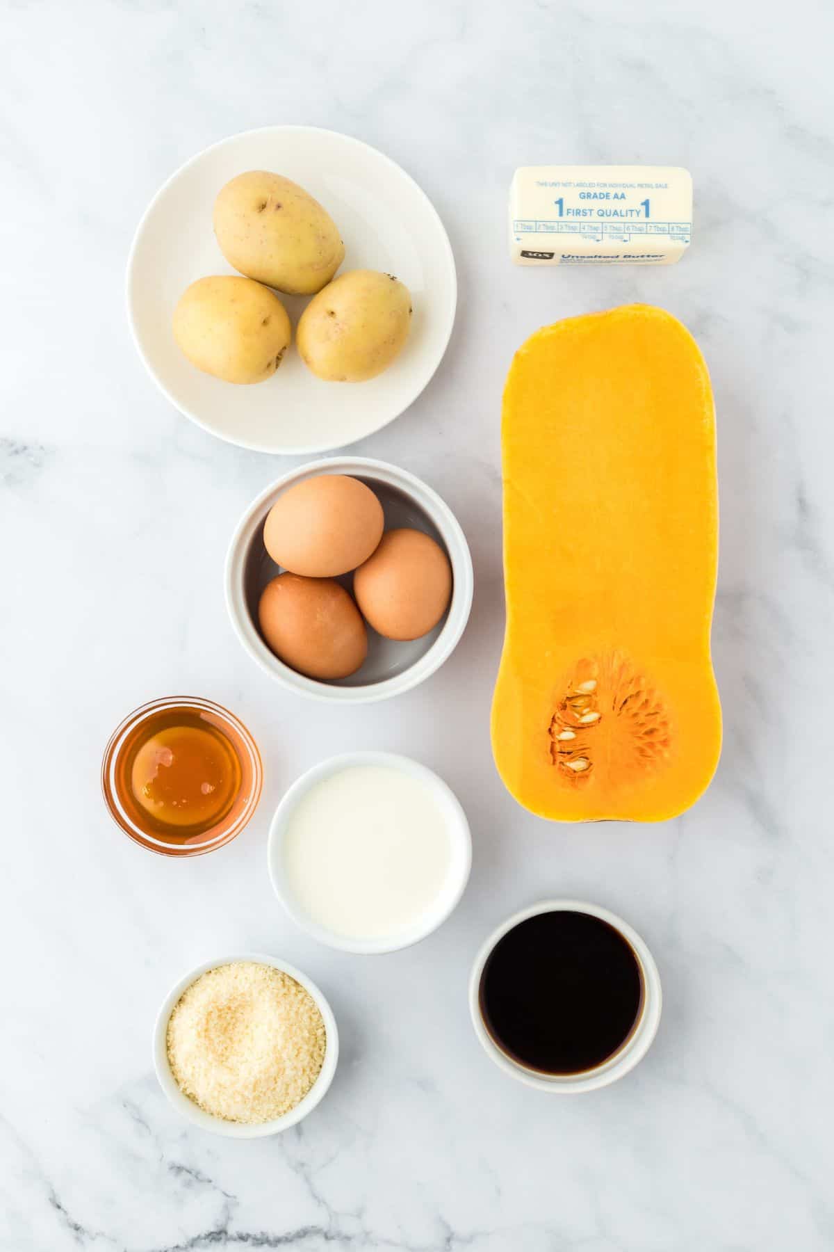 Overhead shot of ingredients for making potato and squash gratin on a marble surface before baking