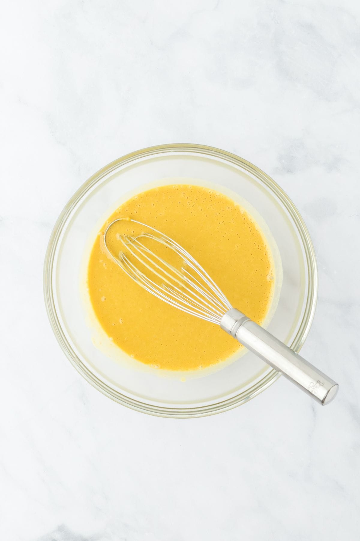 Whisked eggs and squash and potato cream mixture in a glass bowl with a whisk