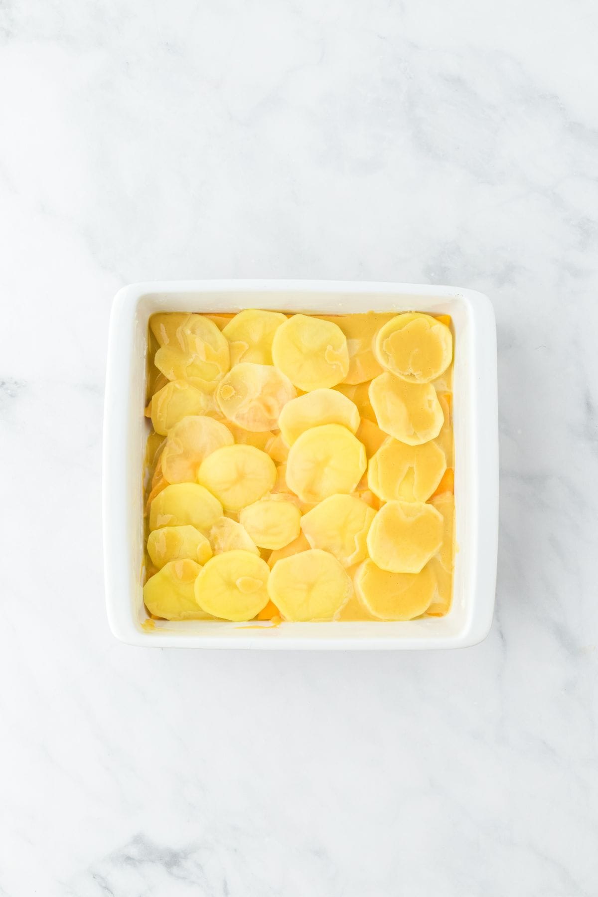 A white baking dish with layered potato slices and butternut squash