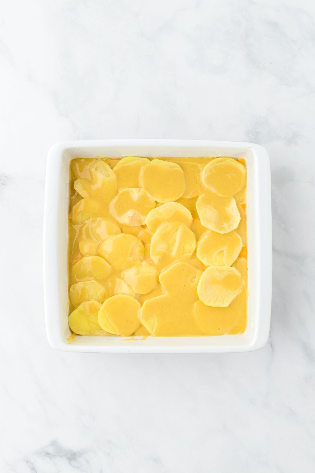 A baking dish with thinly sliced yellow potatoes layered on top of creamy sauce