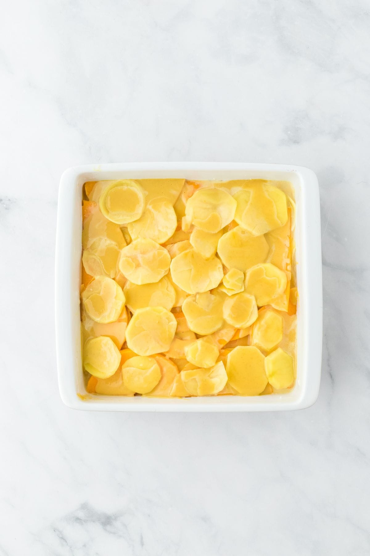 A white baking dish filled with creamy, layered potato slices