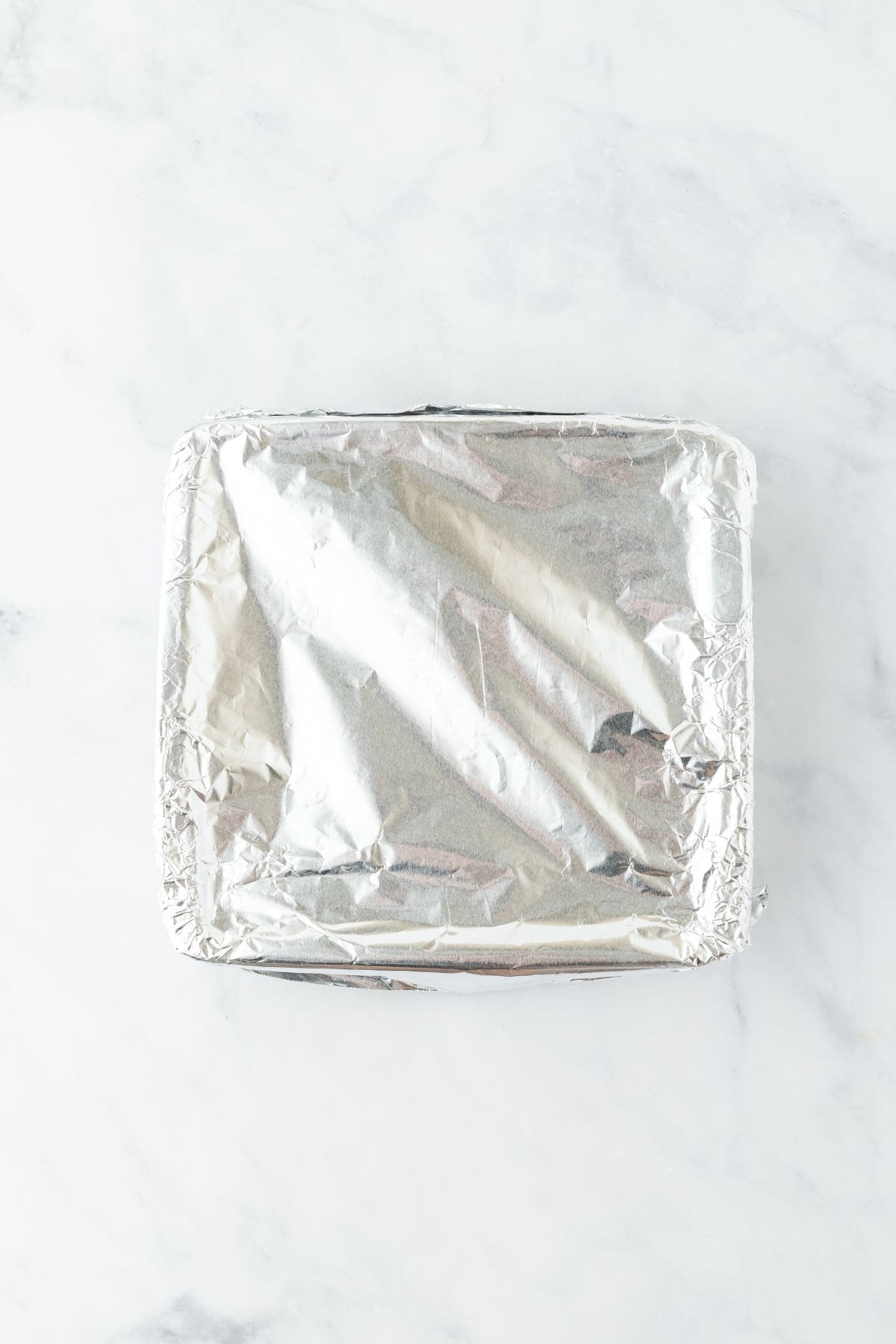 A square baking dish covered with aluminum foil, prepped for baking