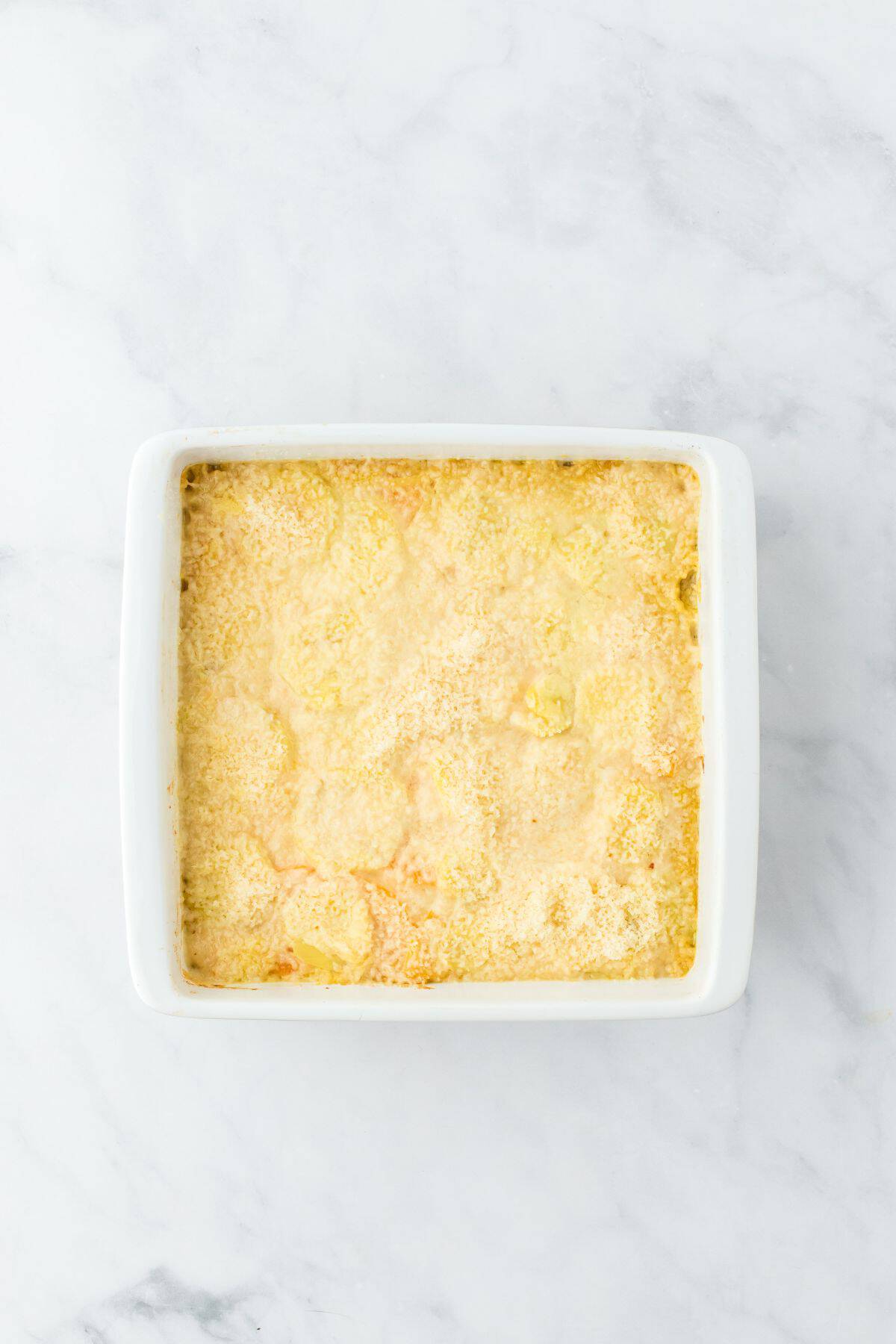 A partially cooked potato and squash gratin, sprinkled with a layer of parmesan cheese, ready for baking