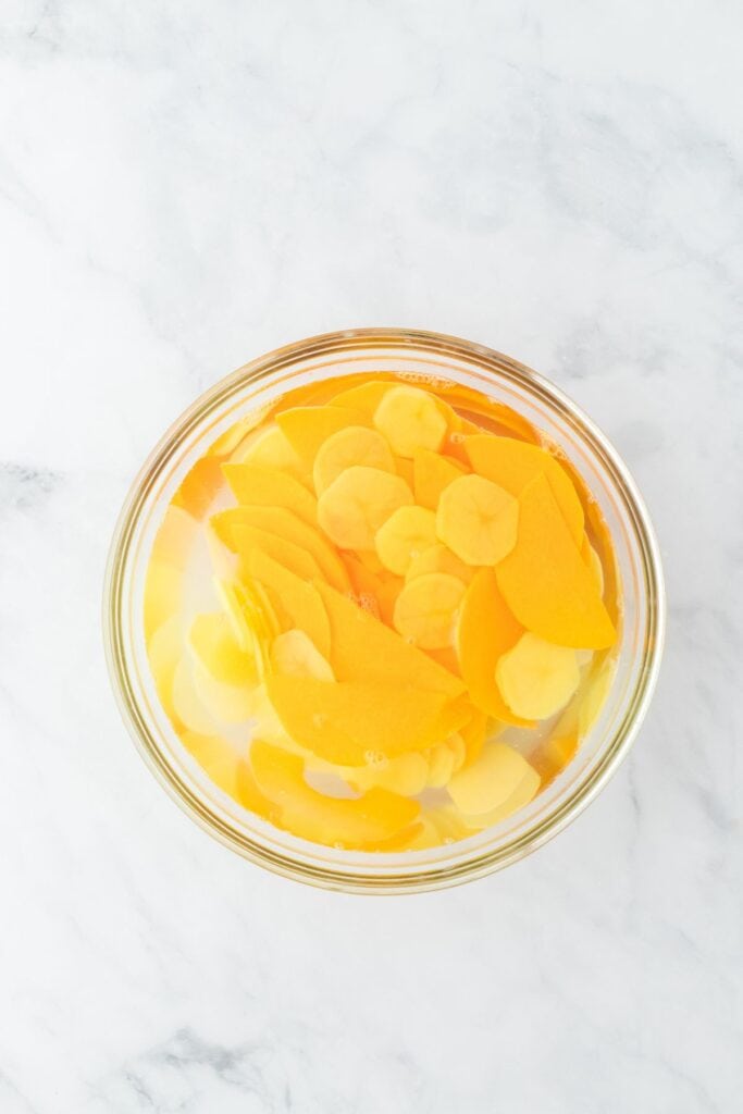 Potato and squash slices soaking in water in a glass bowl