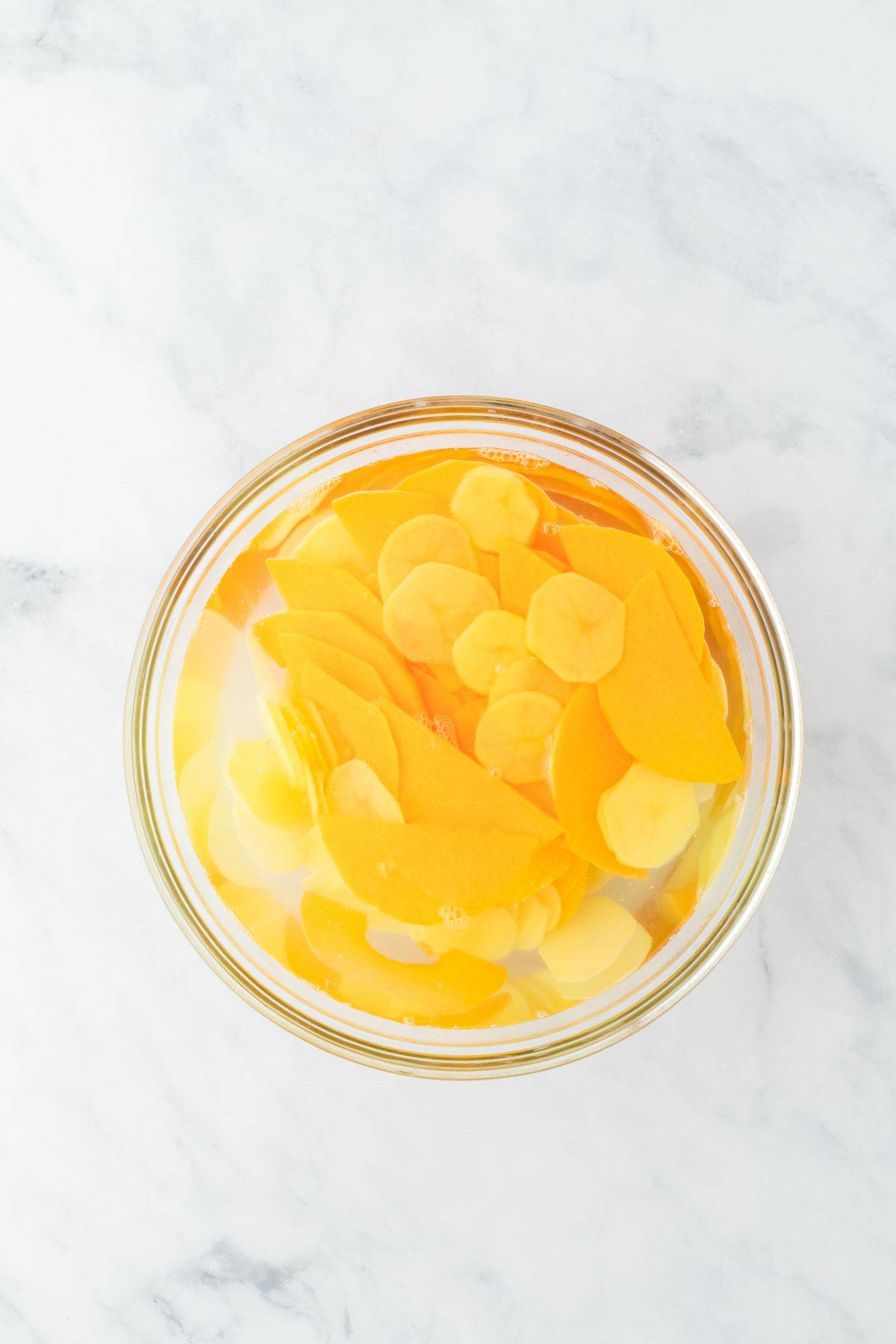 Potato and squash slices soaking in water in a glass bowl