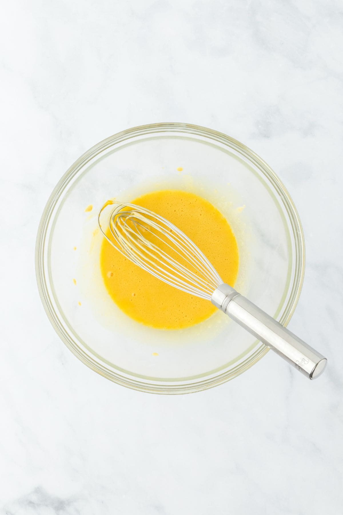 Whisked egg yolks in a glass bowl with a whisk