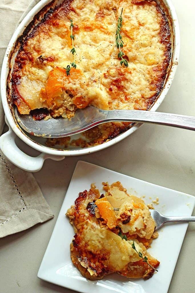 Potato and Squash Gratin served in a white baking pan with a portion scooped out with a serving spoon and a serving placed on a square, white plate with a fork