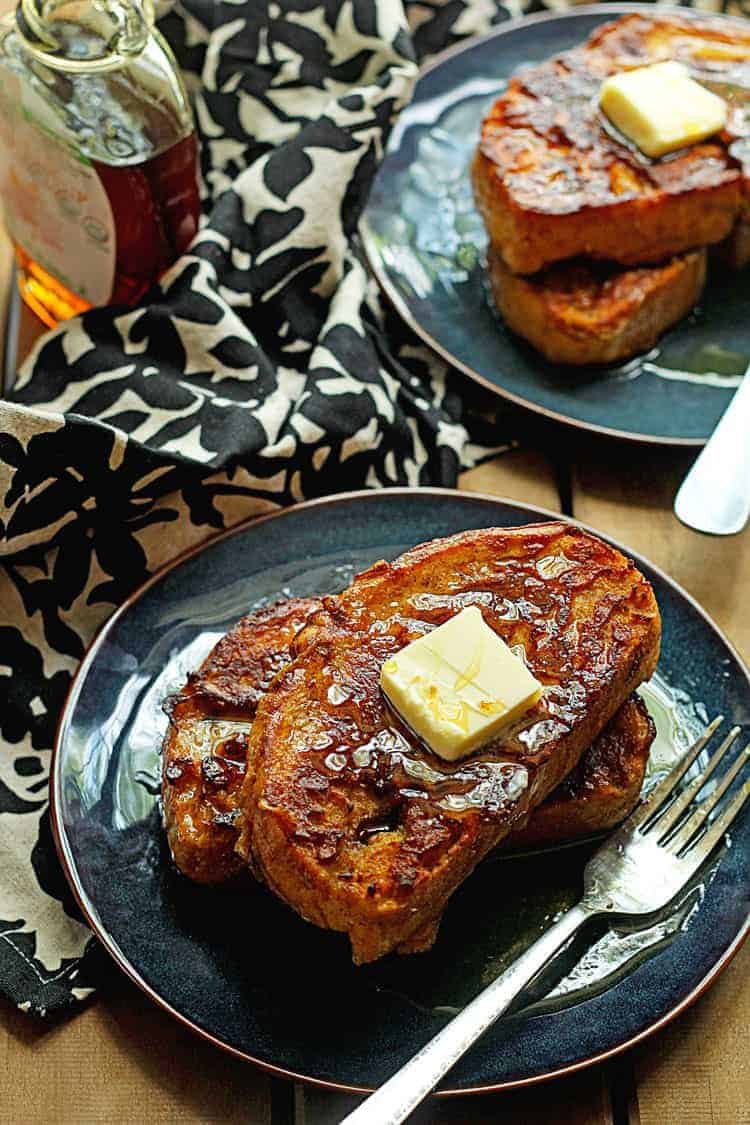 Pumpkin french toast is served on two blue plates with syrup and butter