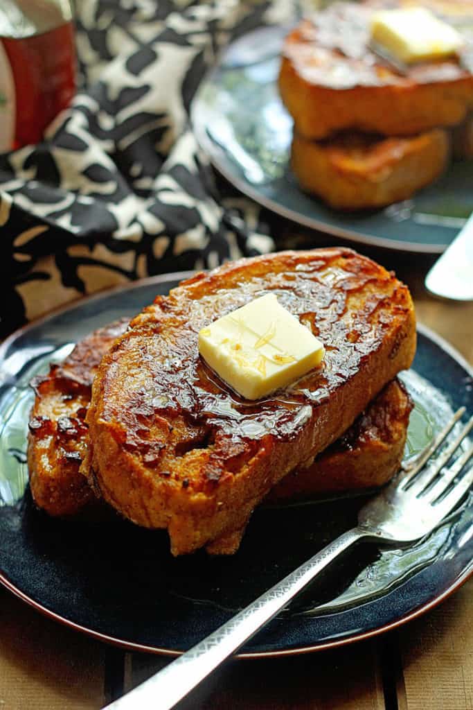 Close up of Pumpkin Spice French Toast with fork on a blue plate with butter and syrup