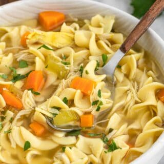 Slow Cooker Chicken Noodle Soup in a white bowl with a spoon digging in