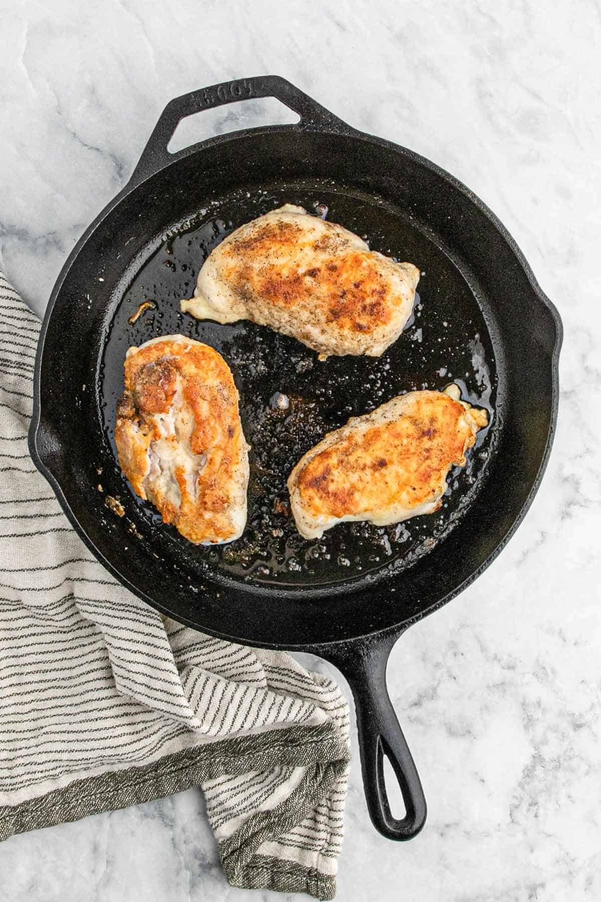 Chicken breasts cooking in a skillet.