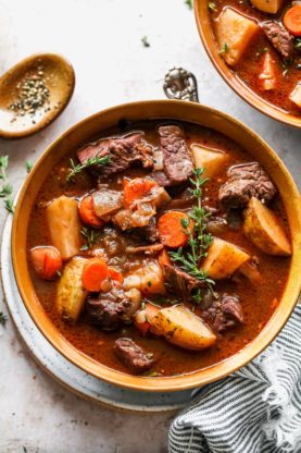 A comforting large orange bowl of beef stew against a white background