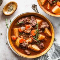 Two orange bowls of beef stew ready to serve with black pepper