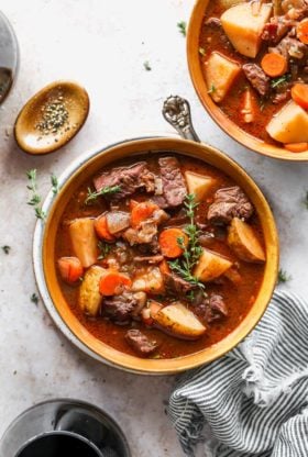 Two orange bowls of beef stew recipe ready to serve with black pepper