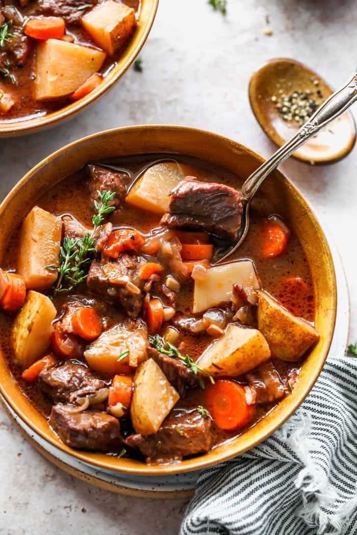 A spoon eating a soup filled with potatoes, carrots and beef