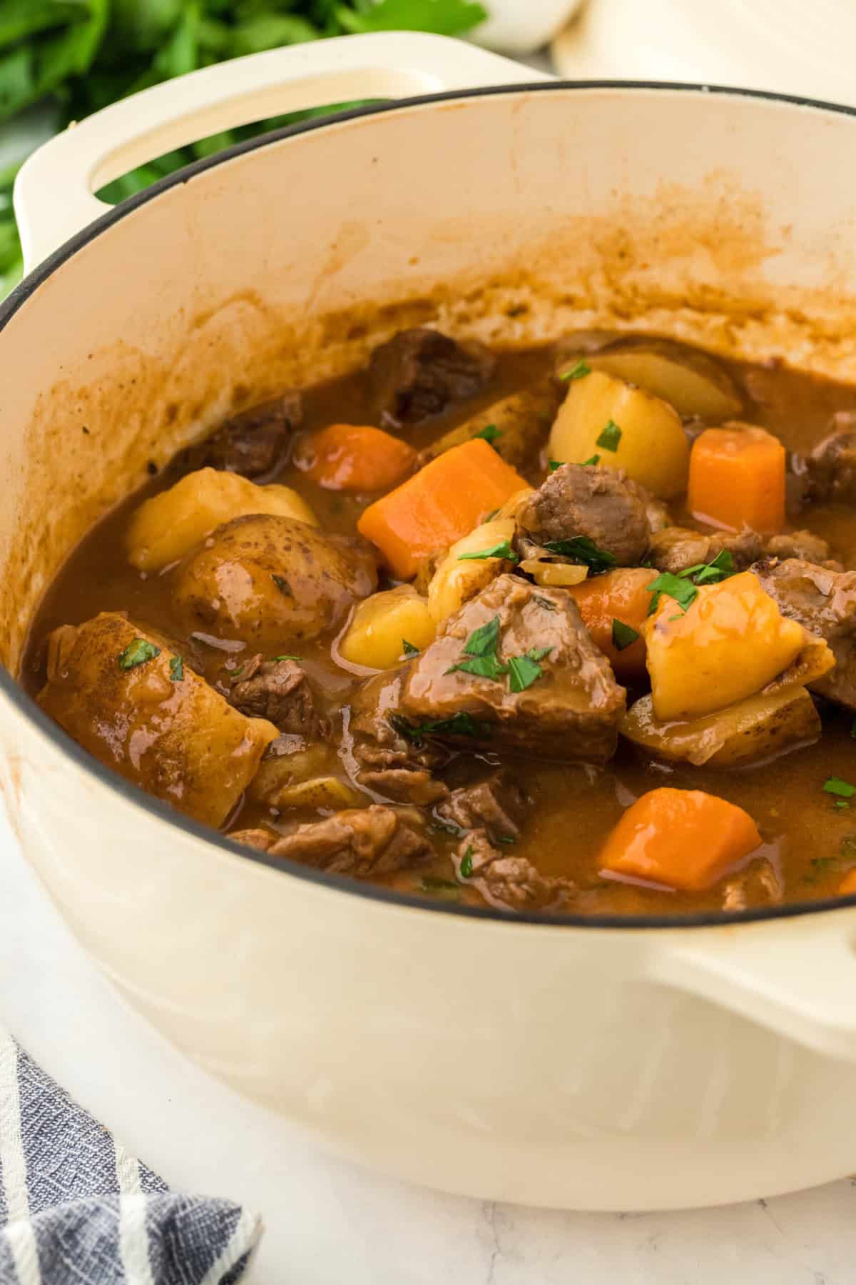 The best beef stew recipe in a large white pot with parsley in the background