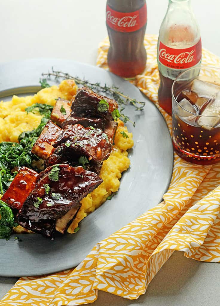 Coke Braised Beef Short Ribs with a sticky sauce on plate with polenta and greens ready to serve