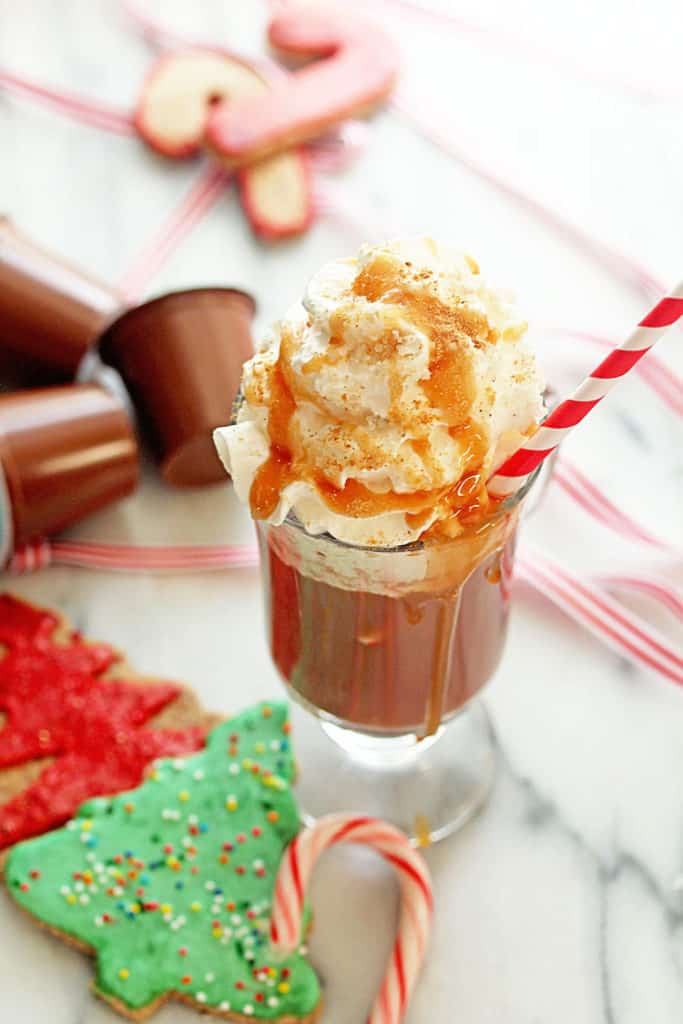 Close up of Salted Caramel Ginger Hot Cocoa served in a glass mug with a white and red striped straw in it and Christmas cookies and a candy cane next to it