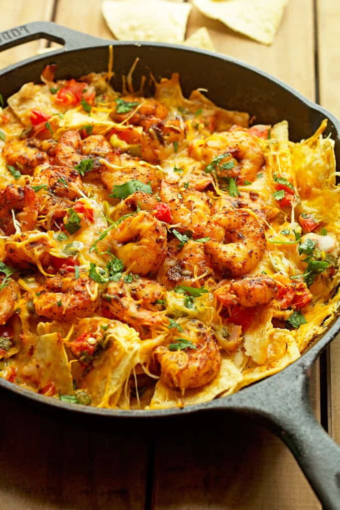 Shrimp sitting on top of nachos recipe in a black cast iron skillet on wooden background 