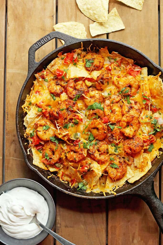 Overhead shot of Shrimp Nachos sitting in a black skillet next to a container of sour cream.