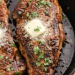Pan seared steaks in a skillet topped with a pat of melting butter.