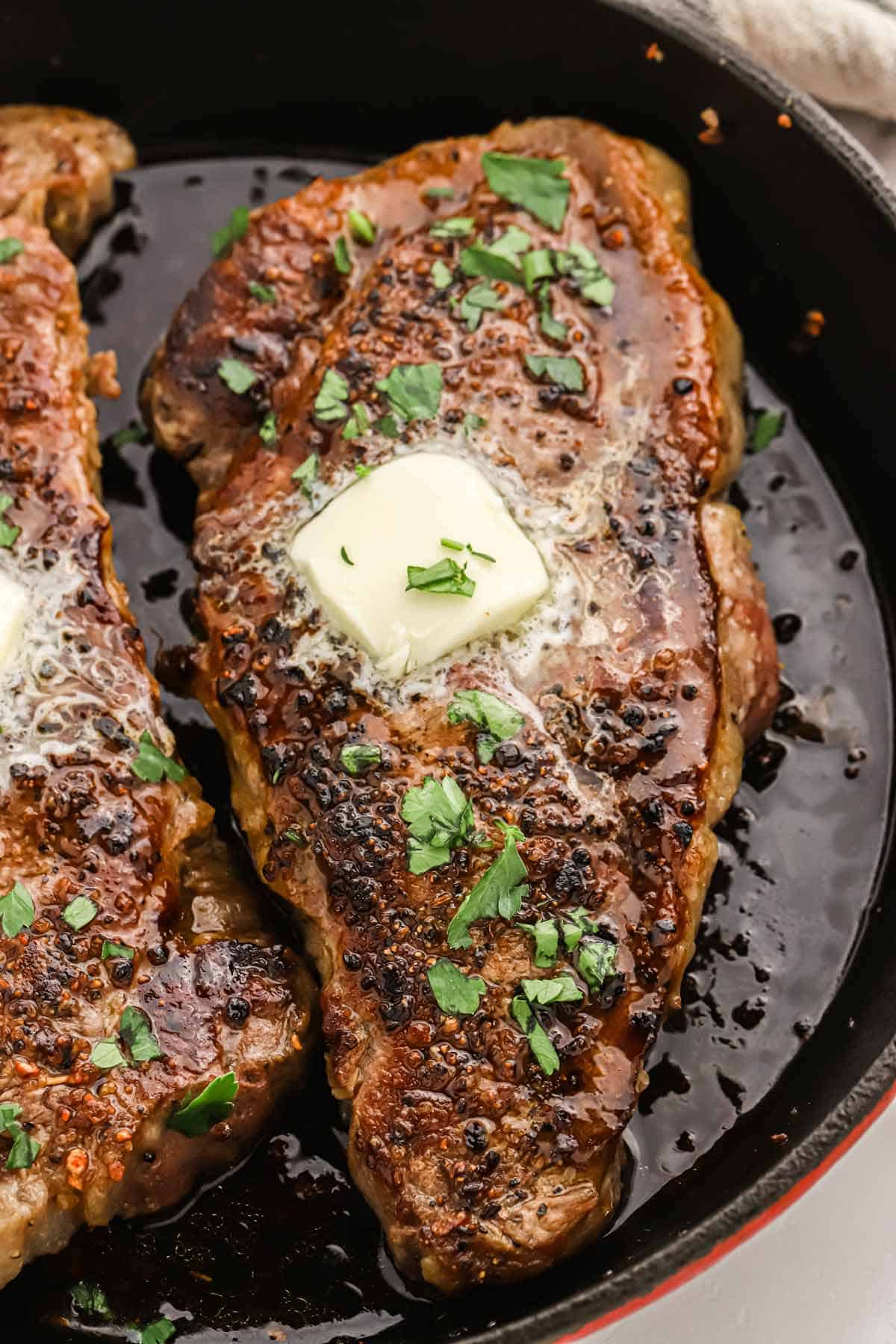 Pan seared steaks in a skillet topped with a pat of melting butter.