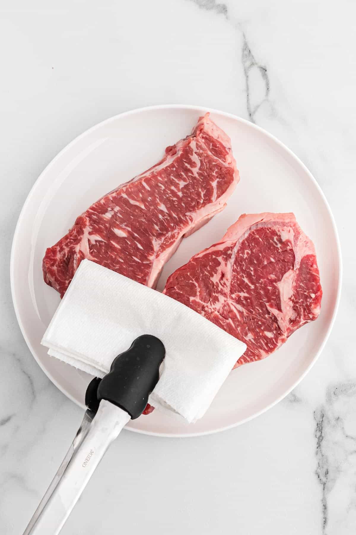 Using a napkin to pat dry steaks on a plate.