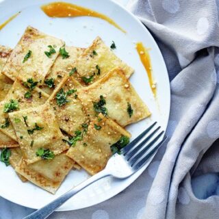 A white plate filled with butternut squash ravioli with a fork on a beige napkin