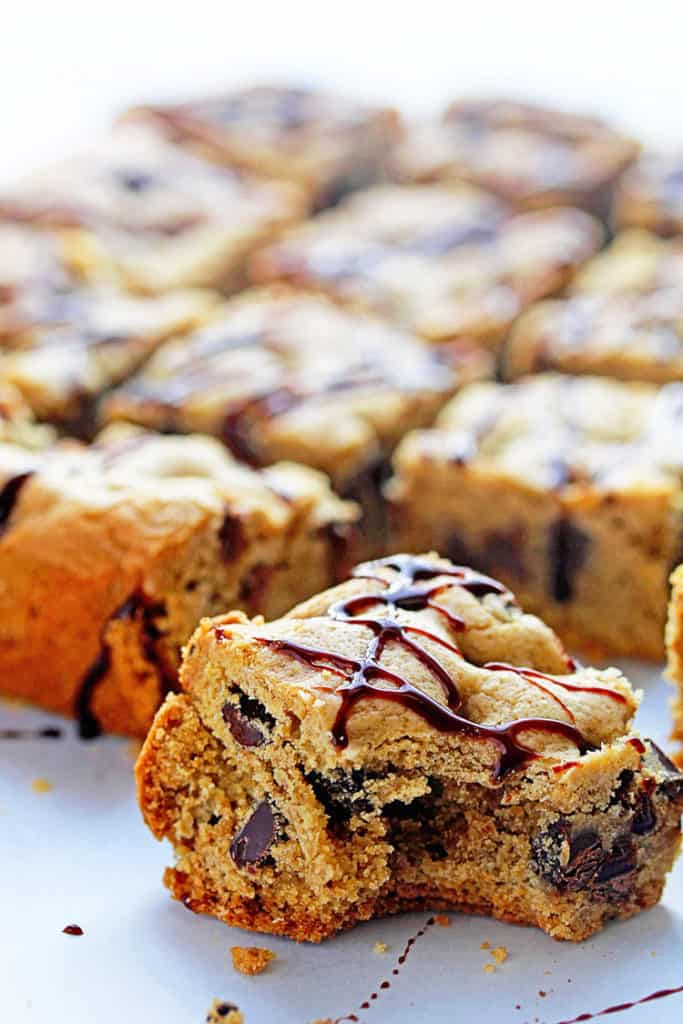 Close up of a chocolate chip cookie bar with a bite taken out of it and several more bars in the background and out of focus