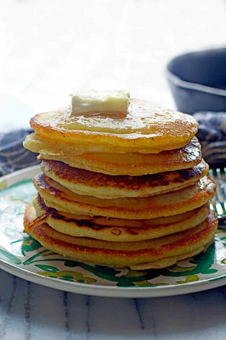 A stack of Hoe Cakes topped with butter and sitting on a green and white plate with a fork