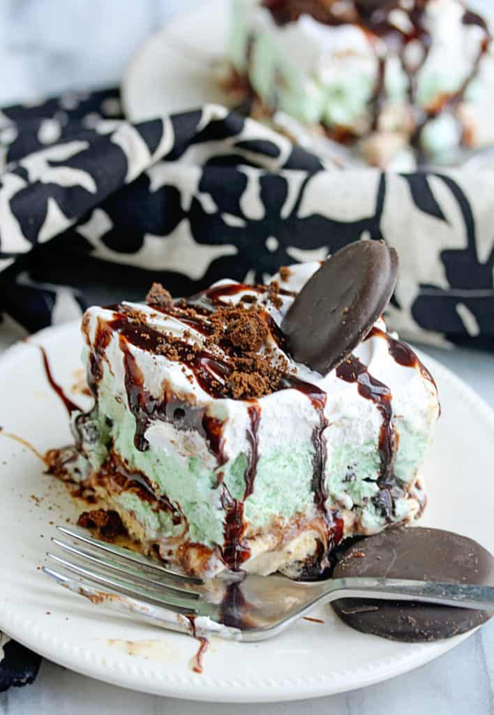 A piece of Girl Scout Cookie Mint Chocolate Ice Cream Cake sitting on a white plate with a fork and another piece in the background