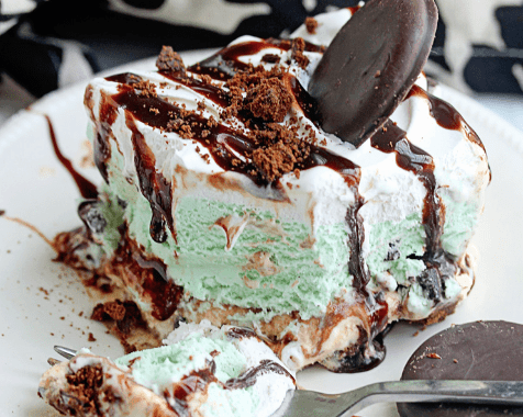 A piece of Girl Scout Cookie Mint Chocolate Ice Cream Cake sitting on a round, white plate with a spoon