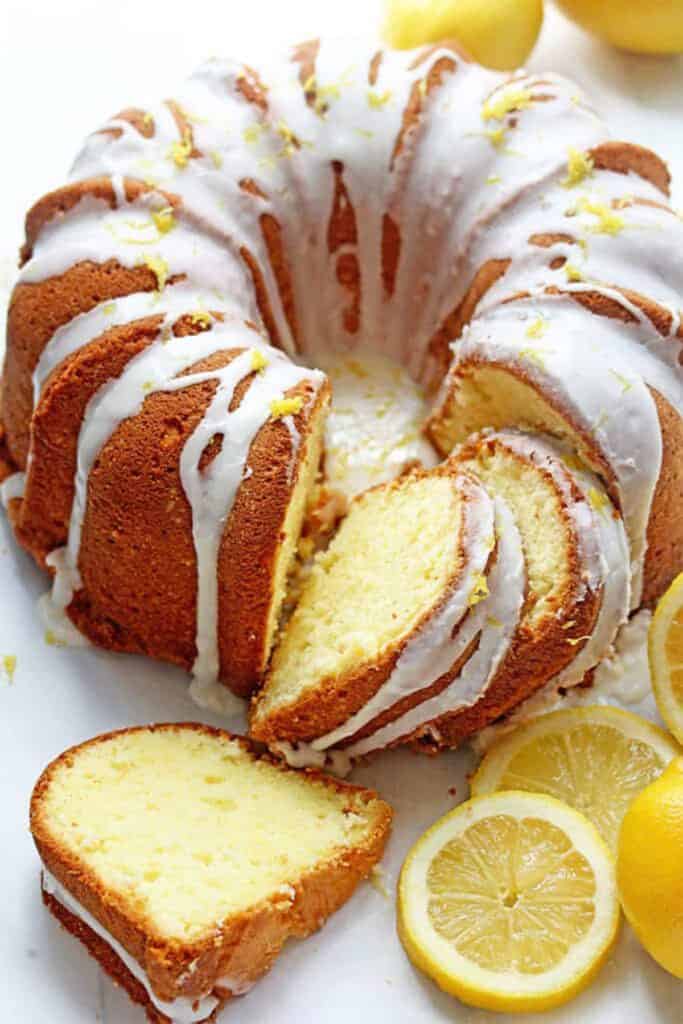 Lemon Cake Recipe with three slices cut out of it and surrounded by lemons and lemon slices